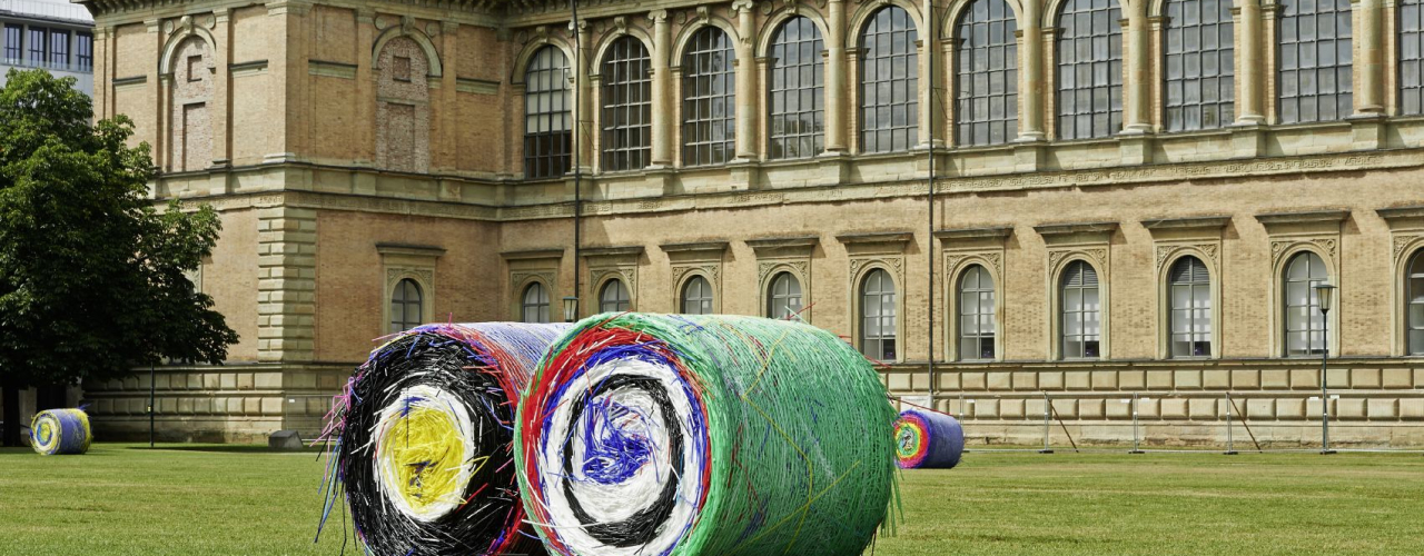 Auf der Wiese vor der Alten Pinakothek liegen zwei riesige bunte Ballen aus Strohhalmen.