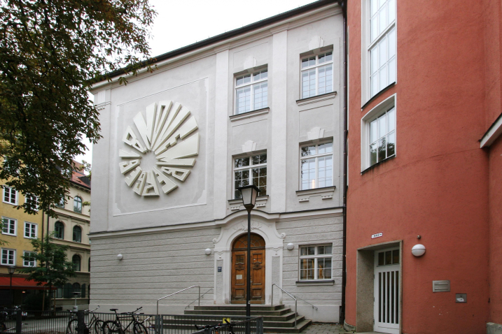 An einer weißen Hauswandfassade ist in Höhe des 1. Stockwerks eine kreisrunde große Installation aus Neonröhren angebracht, die das Datum “8. November 1939“ ergibt.