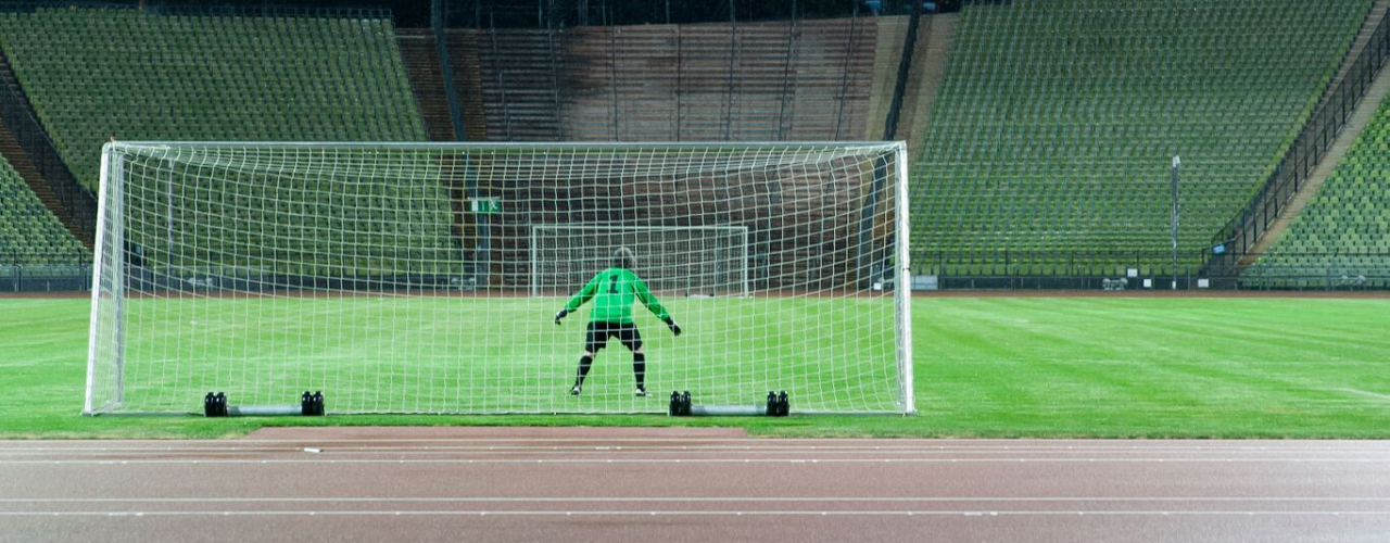 Die Fotografie zeigt das Innere des Olympiastadions bei Nacht. Zu sehen ist der Künstler Massimo Furlan im grün-schwarzen Fußballtrikot in Rückenansicht, der in einem Tor steht. Vor ihm erstreckt sich der grüne Fußballrasen, er ist jedoch der einzige Spieler auf dem Platz. Auf einer Anzeigetafel hoch über den Zuschauerrängen erscheint der Spielstand dieses fiktiven Fußballspiels: "DDR gegen BRD – 0 zu 0".