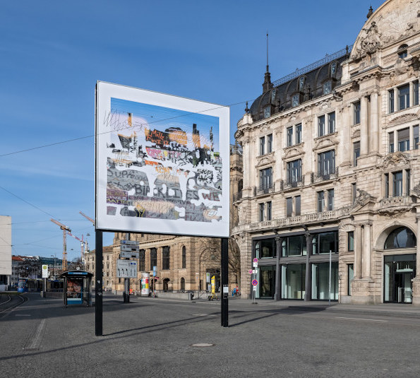 Diagonal view of the billboard. Above a colorful collage of image, word and sign appears barely legible the phrase "Whose Utopia we shall return to".