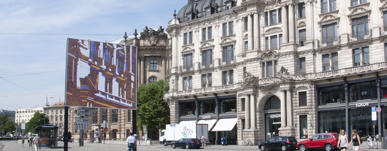 Ansicht des Billboards am Lenbachplatz stadteinwärts blickend mit dem Motiv "hide and seek" von Angela Stauber. Das Motiv gibt gespiegelt das Gebäude rechts neben der Plakatwand wieder. Die architektonischen Formen der historischen Fassade werden mit Hilfe der Technik des Holzschnittes vereinfacht und in eine blockhafte Ästhetik aus farbigen Flächen in den Farben weiß, gelb und blau abstrahiert.
