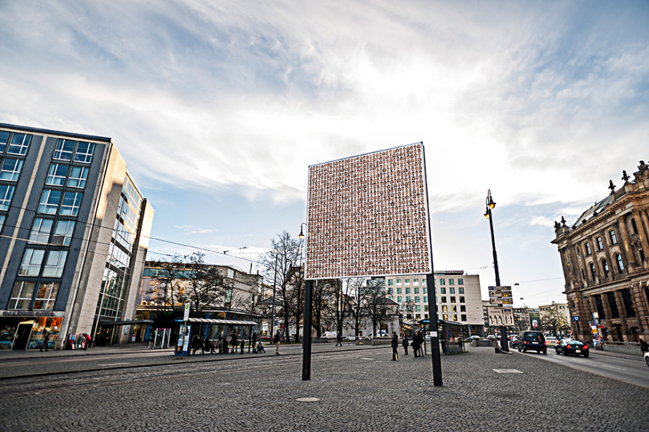 Seitliche Ansicht des Billboards am Lenbachplatz mit dem Motiv "Israelisches Kollektivportrait" von Roland Fischer. Das Motiv zeigt Porträtaufnahmen von Männern und Frauen, die zu Reihen aneinandergesetzt wurden und so den Eindruck eines kollektiven Porträts vermitteln.