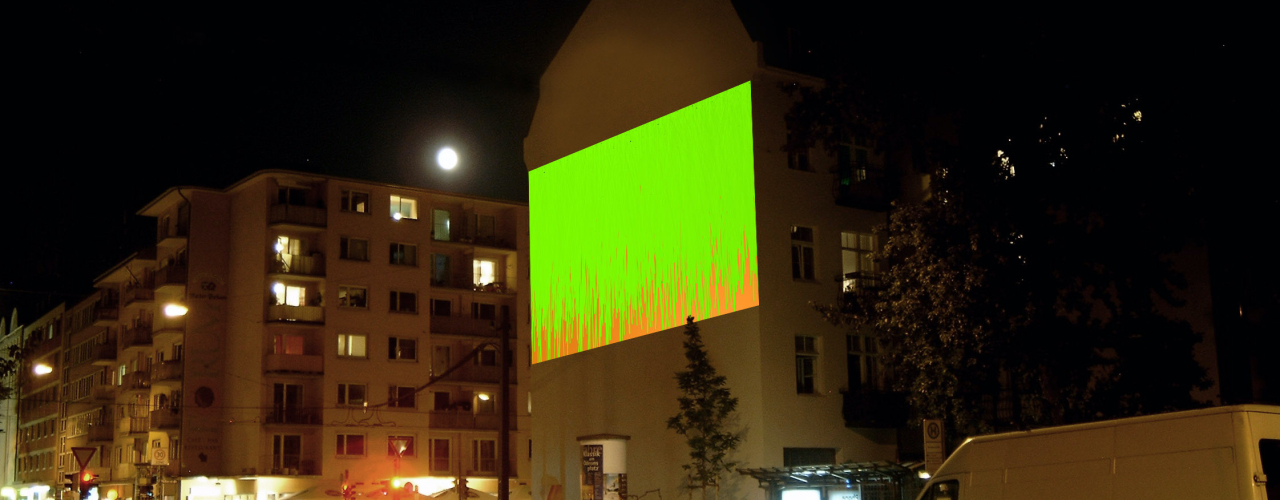 Fotografie der Großprojektion "Bunter Abend" von Wolfgang Aichner und Thomas Huber an einer Gebäudefassade in der Müllerstr. 10 bei Nacht. In der Projektion fließen vom oberen Rand des Projektionsausschnittes zwei Töne zähflüssiger Malfarbe – grün und rot – übereinander.