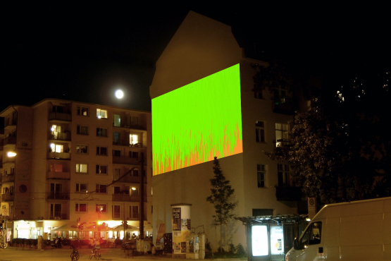 Fotografie der Großprojektion "Bunter Abend" von Wolfgang Aichner und Thomas Huber an einer Gebäudefassade in der Müllerstr. 10 bei Nacht. In der Projektion fließen vom oberen Rand des Projektionsausschnittes zwei Töne zähflüssiger Malfarbe – grün und rot – übereinander.