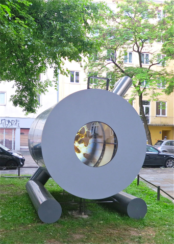 Fotografie einer silberfarbenen Ofenskulptur der Künstlerinnen Alix Stadtbäumer und Yvonne Leinfelder. Diese ist auf der Rasenfläche an der Rumford-Ecke-Klenzestraße platziert. Durch eine Art Bullauge kann man im Inneren des Kunstwerks eine Videoarbeit von Yvonne Leinfelder sehen. Die Skulptur bezieht sich auf eine der wichtigsten Erfindungen des Grafen Rumfords, den sogenannten Rumford-Ofen.