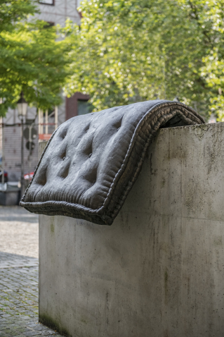 Bild einer Brunnenskulptur von Tatiana Trouvé am Stephansplatz. Die Skulptur besteht aus einem Brozeguss einer Matratze, die über einen Betonsockel gelegt ist.