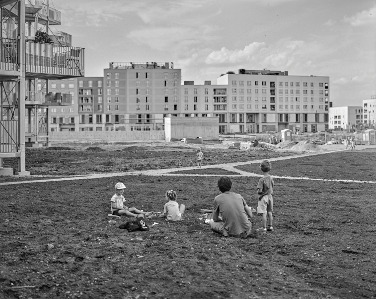 auf der Schwarz-Weiß-Fotografie sind mehrere Kinder und ein Erwachsener sitzend bzw. stehend vor Freihamer Neubauten zu sehen, Reste einer Baustelle wie ein Dixi-Klo und Erdhaufen sind noch zu sehen