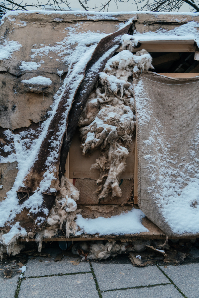 Detailaufnahme der Lehmskultur in Form eines SUV. Die Struktur aus Lehm, Stoff und Dämmmaterial ist teilweise beschädigt und von einer dünnen Schneeschicht bedeckt.
