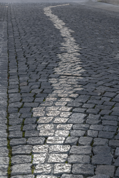 Detailaufnahme einer gepflasterten Fläche, ein Streifen mit einer Breite von ein bis vier Steinen hebt sich durch eine gold-glänzende Oberfläche ab.