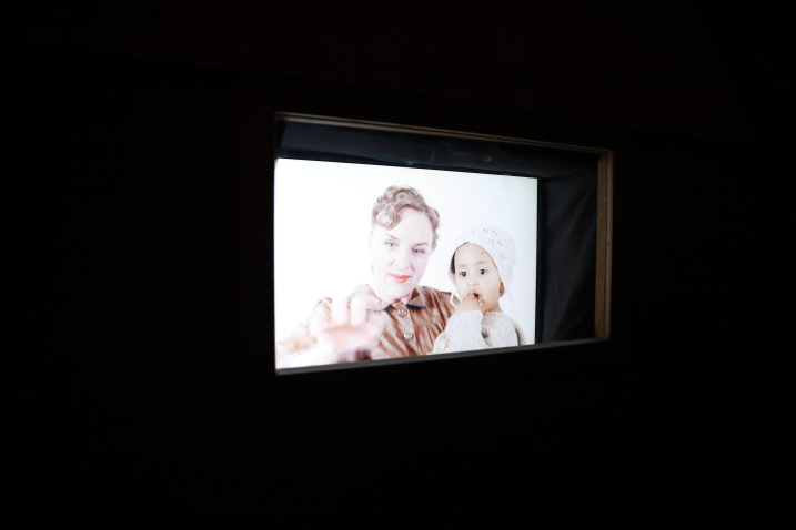 Oblique view of a screen in a dark room, showing a blonde woman holding a child with darker skin and brown eyes.