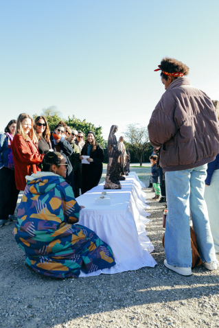 A group of people are standing outdoors around a table covered with white cloths and sculptures.