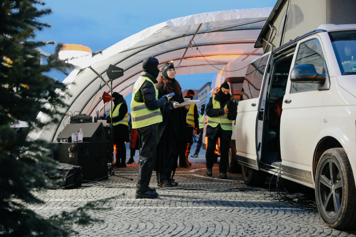 Several people, some of them wearing masks and high-visibility vests, are working at a mobile station next to a white van under a tent.